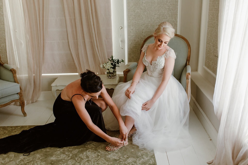 Bridesmaid Helping Bride with Shoe | Image: Jenni Elizabeth